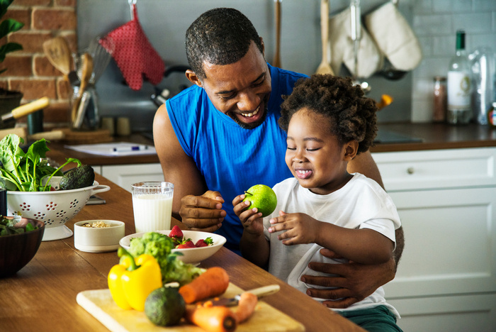 A man is smiling as he is looking at a child in his arms. The child is smiling at a vegetable in their hand.