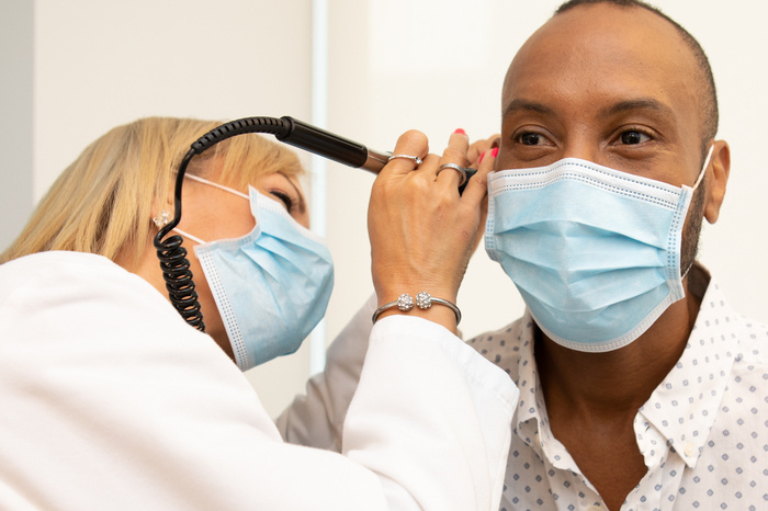 doctor looking into the ear of a patient. Both the doctor and patient are wearing masks. 