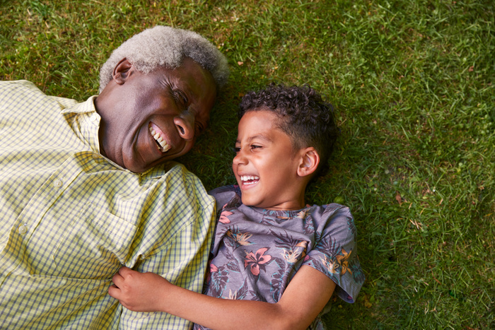 Man and young boy laying in the grass smiling to one another. 
