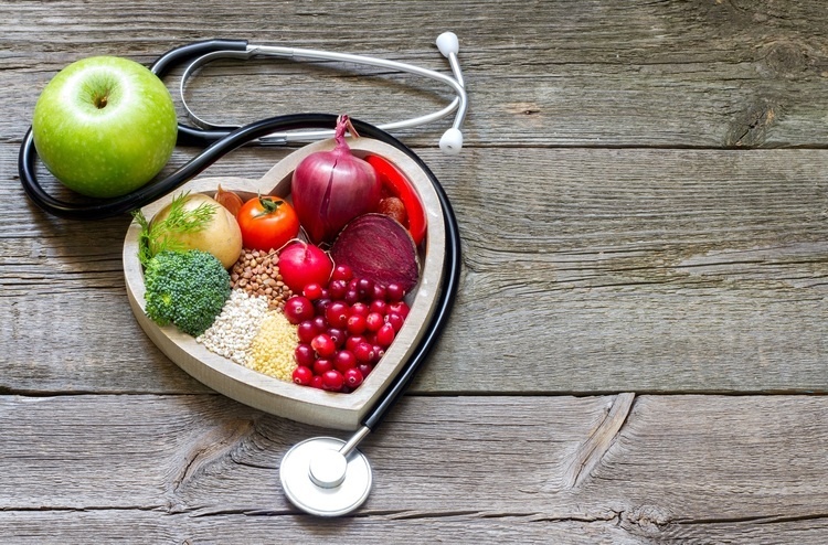 stethoscope wrapped around heart shaped wooden bowl with fruits and vegetables inside.