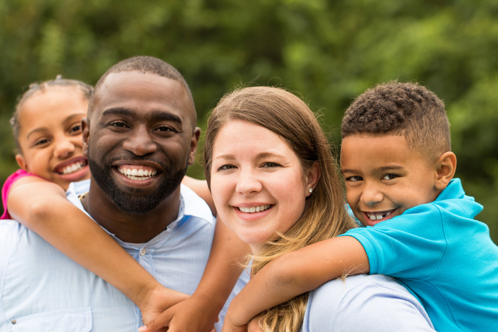 Mother and father holding children on their back. All smiling at the camera.