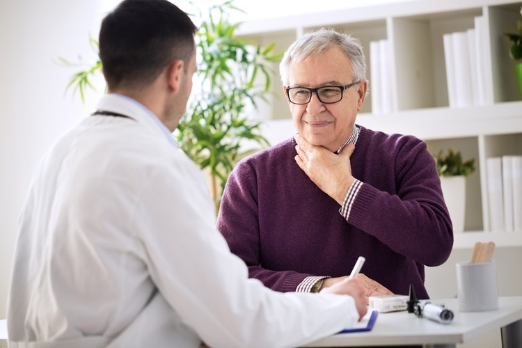 Older male holds throat indicating discomfort. Doctor is facing patient.
